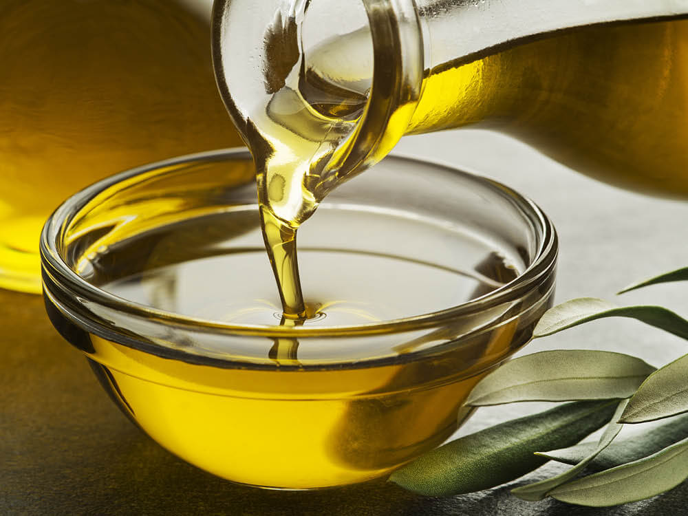 pouring olive oil from a bottle in to a glass bowl with olive leaves in the foregraound