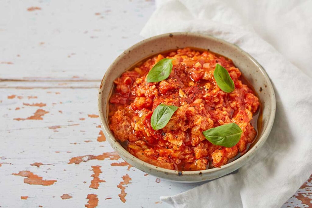 an earthenware bowl containing a simple yet tasty Italian peasant dish, called Pappa al Pomodoro, set on a white distressed table